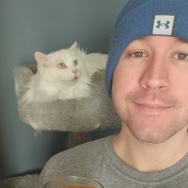 Caleb, with his cat behind him and an iced coffee in hand